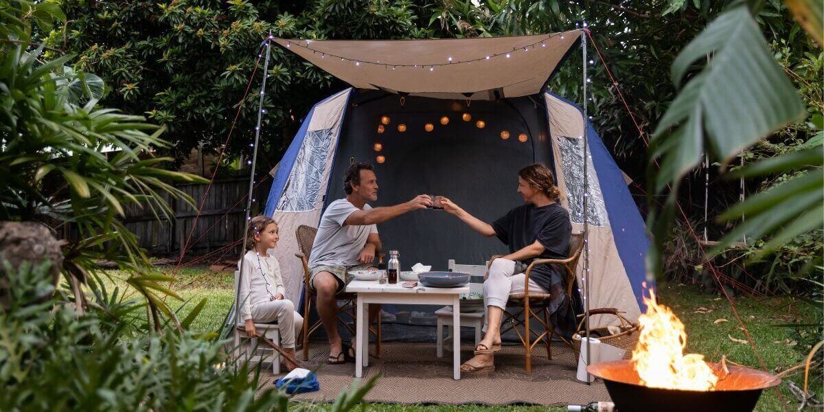 Family enjoying a backyard camping experience with a tent, fire pit, and outdoor seating.